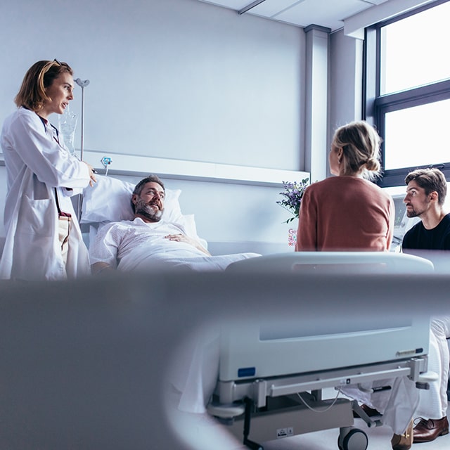 Patient in a hospital bed surrounded by a doctor (left of patient) and two people (right of patient)